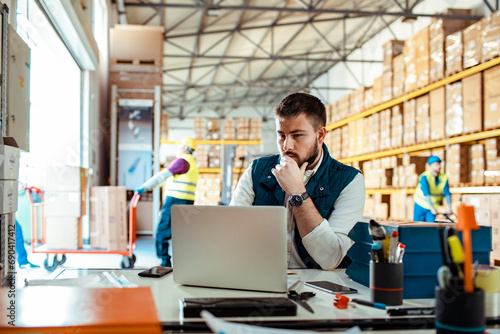 Professional male manager using laptop in warehouse photo