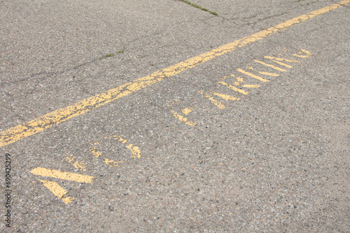 no parking caption print text writing in yellow below line on pavement, worn and faded, shot on angle going diagonal