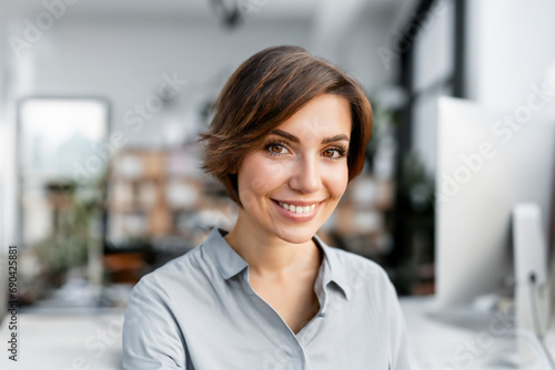 Portrait einer jungen Frau mit braunen Augen und kurzen dunklen Haaren die zuhause im Home Office Büro in die Kamera lächelt photo