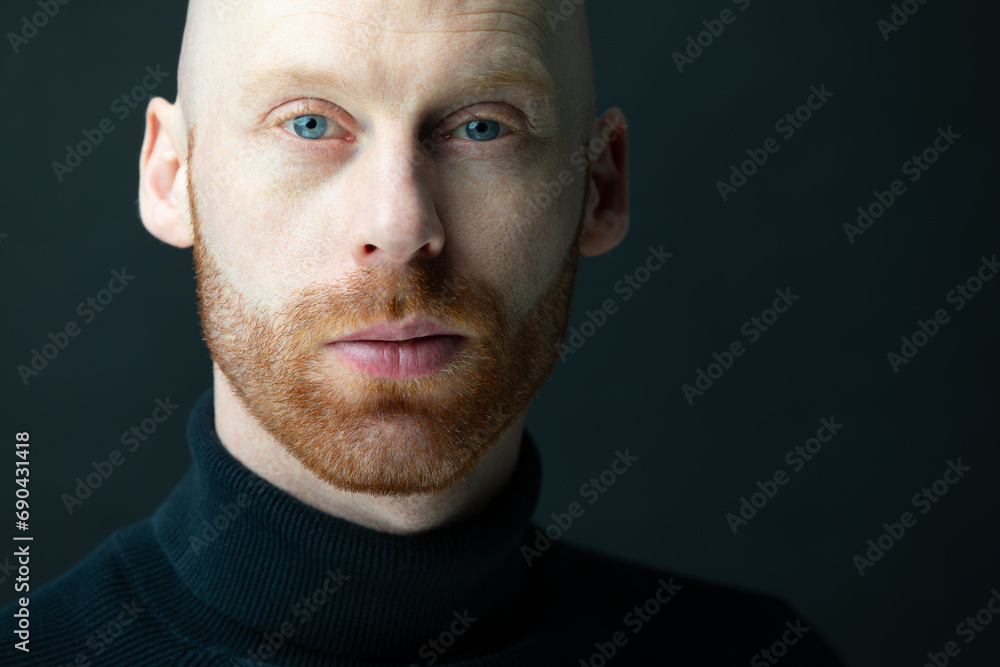 Mann mit Glatze,einem roten haarigen 3-Tage-Bart blickt selbstbewusst und stark mit seinen blauen Augen bekleidet mit einem Rollkragenpullover selbstsicher, vor einem schwarzen Hintergrund, in die cam - obrazy, fototapety, plakaty 