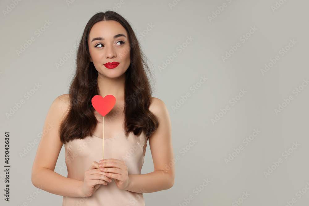 Beautiful young woman with paper heart on grey background, space for text Beautiful young woman with paper heart on grey background, space for text