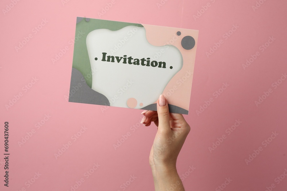 Woman holding beautiful card with word Invitation on pink background, closeup Woman holding beautiful card with word Invitation on pink background, closeup
