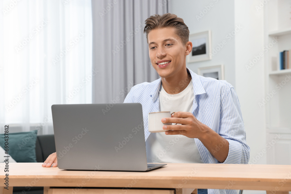 Happy young man having video chat via laptop at wooden table indoors Happy young man having video chat via laptop at wooden table indoors