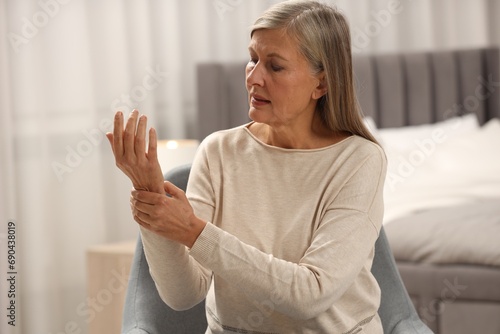 Mature woman suffering from pain in hand at home, space for text. Rheumatism symptom photo