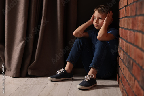 Child abuse. Upset boy sitting on floor near brick wall indoors, space for text