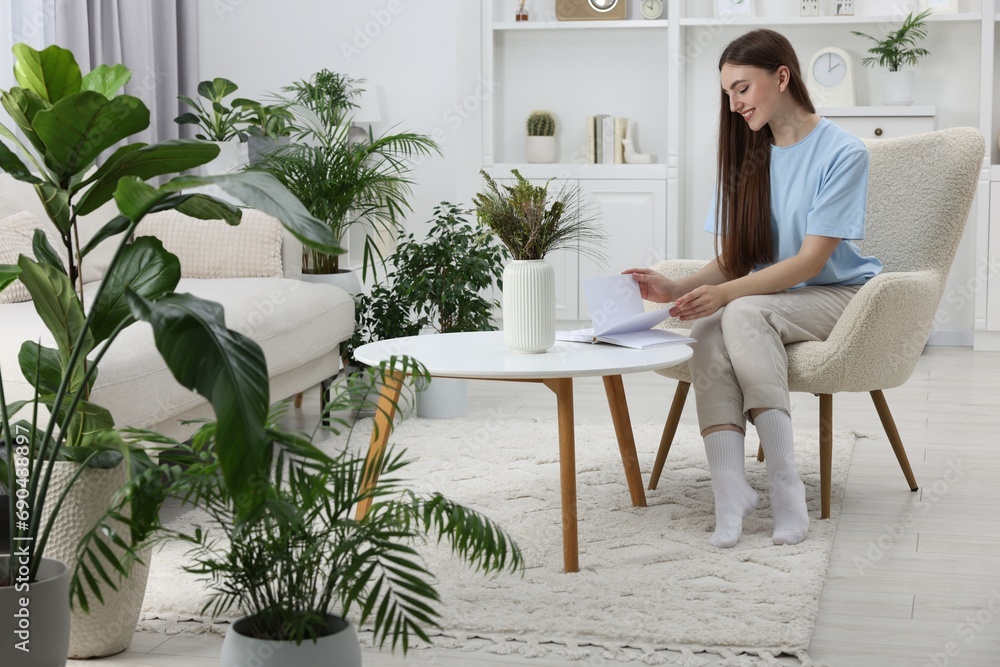 Beautiful young woman with book at table in room with green houseplants Beautiful young woman with book at table in room with green houseplants