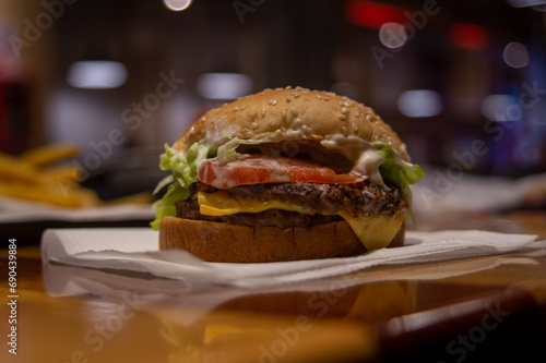 hamburguesa con queso, tomate y lechuga, sobre una servilleta blanca en un restaurante de comida rápida efecto bokeh