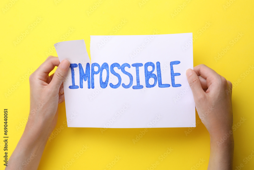 Motivation concept. Woman making word Possible from Impossible by tearing paper on yellow background, top view