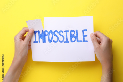 Motivation concept. Woman making word Possible from Impossible by tearing paper on yellow background, top view photo