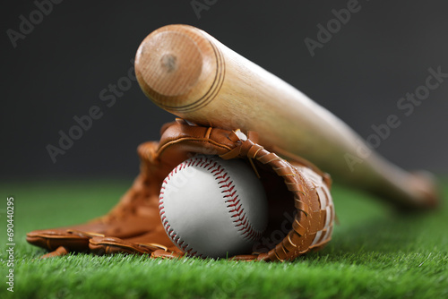 Baseball bat, leather glove and ball on green grass against dark background, closeup photo