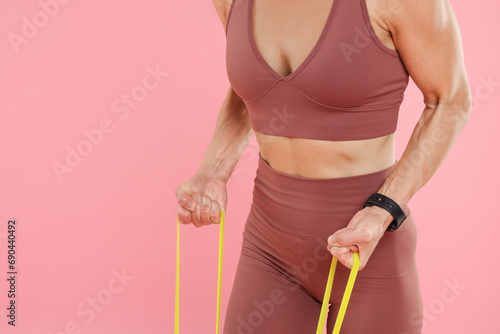 Woman exercising with elastic resistance band on pink background, closeup. Space for text