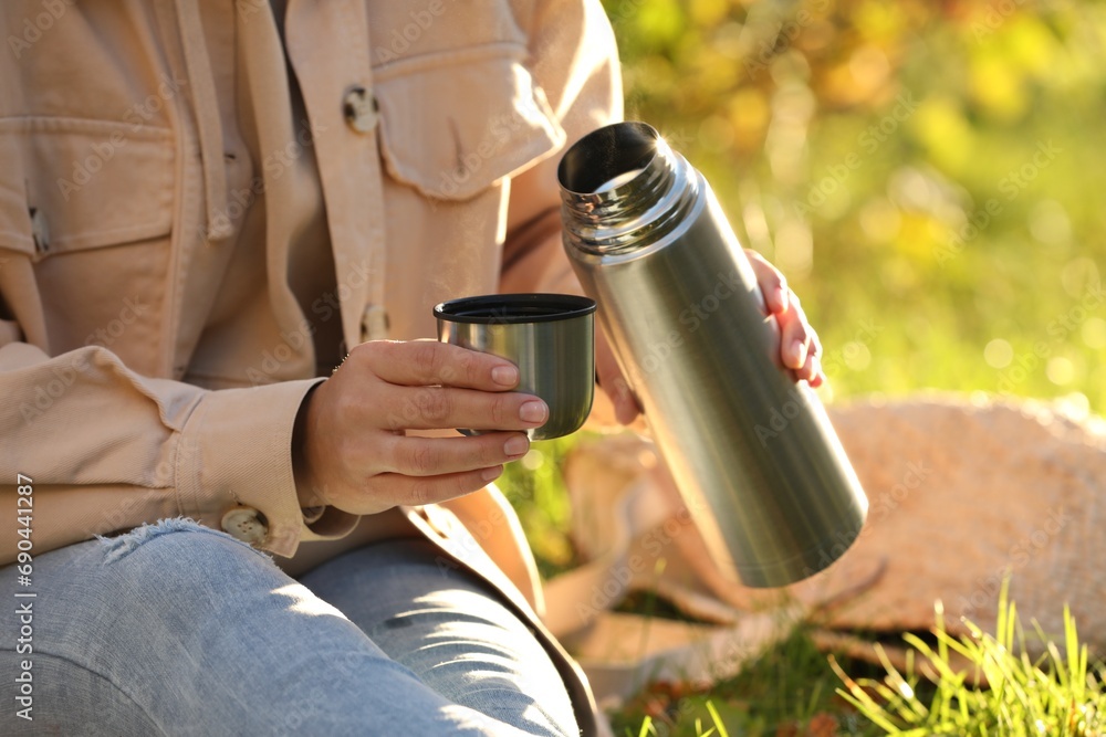 Fototapeta premium Picnic time. Woman with thermos and cup lid on green grass outdoors, closeup
