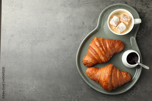 Tasty croissants served with cup of hot drink on grey textured table, top view. Space for text