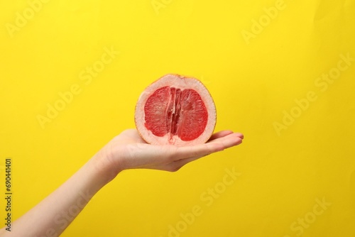 Woman holding half of grapefruit on yellow background, closeup. Sex concept
