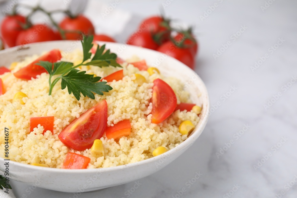 Tasty couscous with parsley, corn and tomatoes in bowl on white marble table, closeup. Space for text