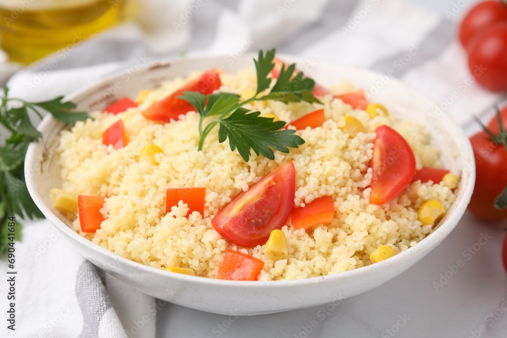 Tasty couscous with parsley, corn and tomatoes in bowl on white table, closeup Tasty couscous with parsley, corn and tomatoes in bowl on white table, closeup
