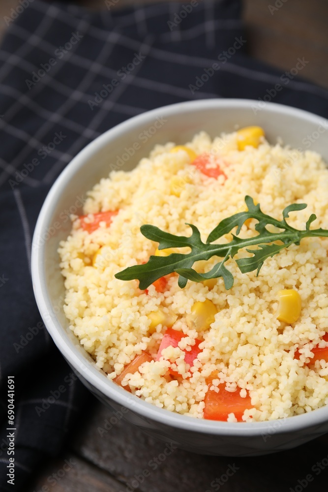 Tasty couscous with pepper, corn and arugula in bowl on wooden table, closeup Tasty couscous with pepper, corn and arugula in bowl on wooden table, closeup