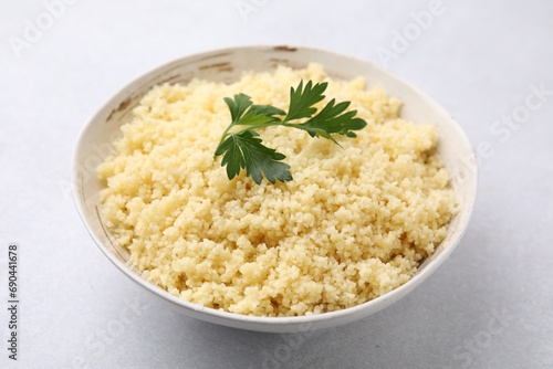 Tasty couscous and fresh parsley in bowl on light grey table, closeup