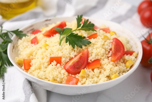 Tasty couscous with parsley, corn and tomatoes in bowl on white table, closeup