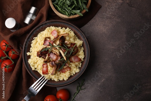 Tasty couscous with mushrooms and bacon in bowl served on brown table, flat lay. Space for text