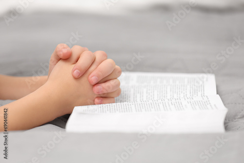 Obraz na plátně Girl holding hands clasped while praying over Bible indoors, closeup