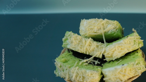 Bolu pandan kukus or chocolate pandan steamed sponge with cheese topping placed on a small plate on a plain background.