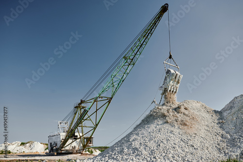 Walking excavator pours chalk from bucket against blue sky