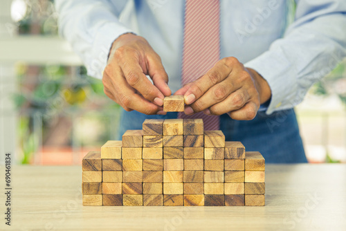 Hand placing wooden block tower stack in pyramid stair step with caution to prevent collapse or crash concepts of financial risk management and strategic planning and business challenge plan.