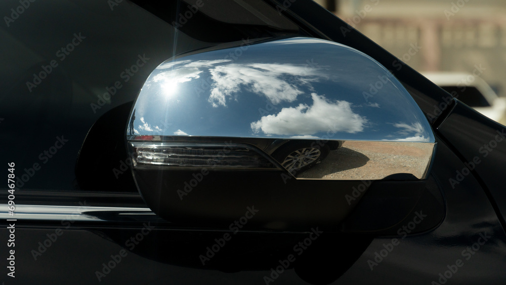 Luxury of black car side mirror that was folded down while parking. Park your car in an open area. Reflection of the sky in the chrome side mirror frames.