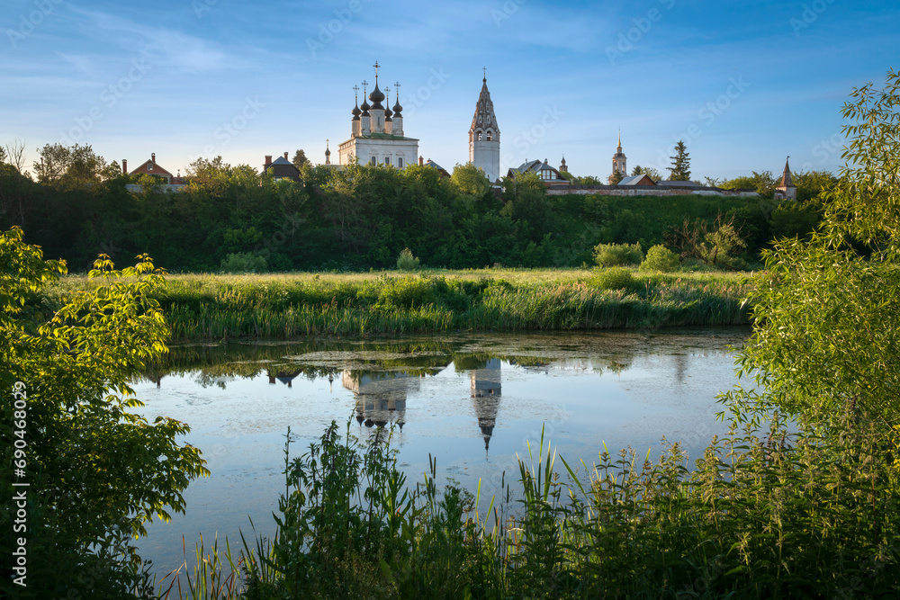 View of the Church of the Ascension of the Lord with a bell tower in the Alexander Monastery on the banks of the Kamenka River on a sunny summer day, Suzdal, Vladimir region, Russia