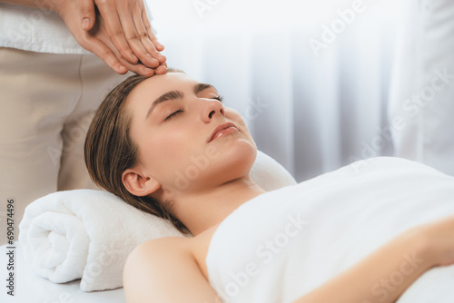 Caucasian woman enjoying relaxing anti-stress head massage and pampering facial beauty skin recreation leisure in dayspa modern light ambient at luxury resort or hotel spa salon. Quiescent