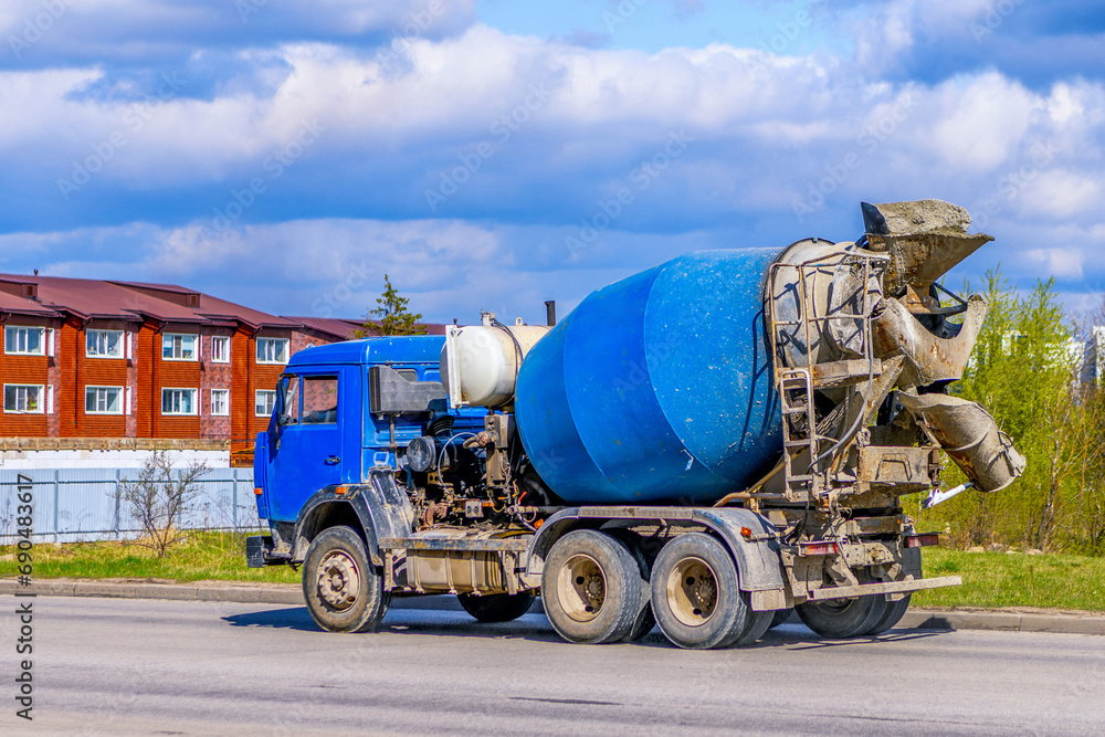 A large automobile concrete mixer drives along the road to a construction site. Blue concrete truck against a background of a beautiful sky.