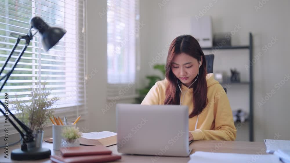 Asian female student engages in focused online learning using her laptop and headphones. She diligently records study materials in a notebook at her home workspace. Asian female student engages in focused online learning using her laptop and headphones. She diligently records study materials in a notebook at her home workspace.
