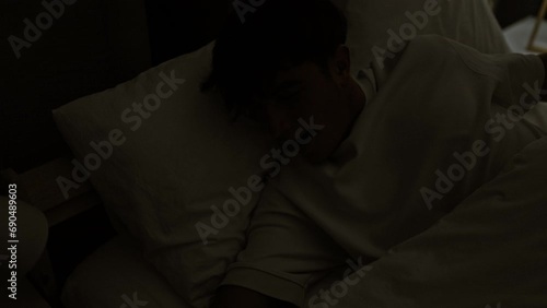 Happy young hispanic teenager stretching arms in comfort of his morning bed, waking up confidently in a well-lit bedroom photo