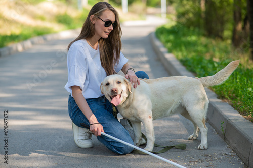 Blind young woman cuddling with guide dog on a walk outdoors. 