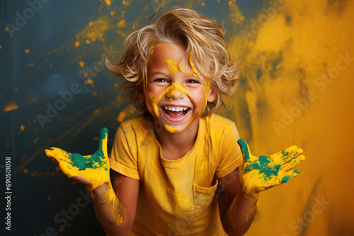 A happy child, smeared with yellow and green paint, laughs joyfully directly at the camera against a colorful studio background. Childhood concept.