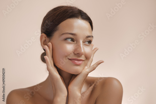 Happy beautiful young adult woman showing her perfect face with healthy shiny skin. Beauty photo of gorgeous girl after morning beauty cosmetic routine finishes daily makeup on pink background. Youth