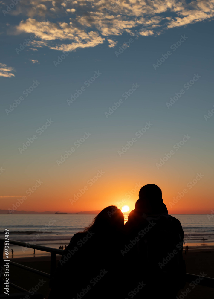 Couple in Love Sitting on Pier Watching Setting Sun, Huntington Beach, California, USA, vertical