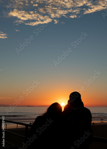 Couple in Love Sitting on Pier Watching Setting Sun, Huntington Beach, California, USA, vertical