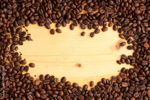 Top view of roasted coffee beans texture background on flat lay in horizontal with wooden board free space in center. pattern for design menu drink. coffee beans frame.