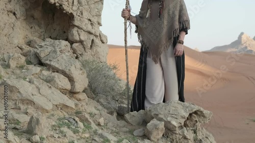 A young bearded shaman with a staff in his hand walks along the rocks in the middle of the desert photo