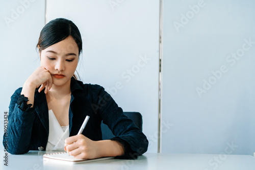 Beautiful young Asian woman writes letter on notebook while sitting at office desk. Content writer and secretary job concept. uds photo