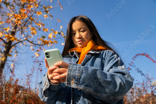 young girl of asian culture using smart phone in the street autumn station
