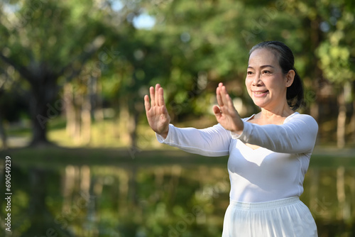 Portrait of mindful senior woman practicing Tai Chi outdoor near lake at summer park