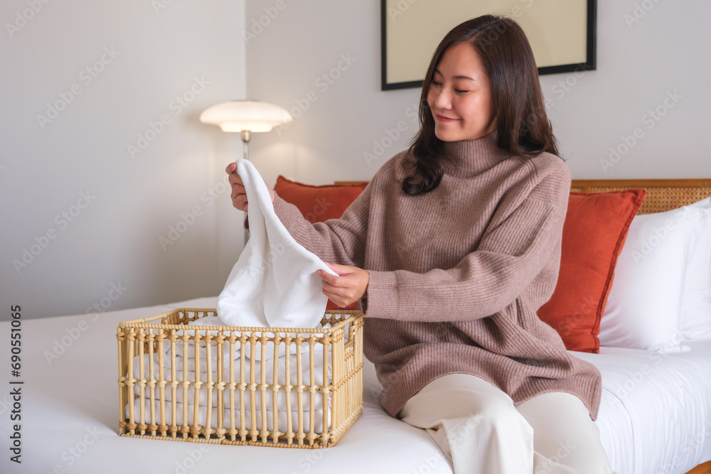 Portrait image of a young woman folding and putting towel into a wooden basket at home Portrait image of a young woman folding and putting towel into a wooden basket at home