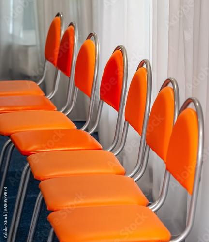 Orange chairs with a metal frame in the lecture hall against the background of window curtains