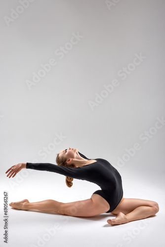 Beautiful flexible talented motivated gymnast wearing black bodysuit working out dancing posing sitting in splits doing backbend art gymnastics exercise white background copy space flexibility