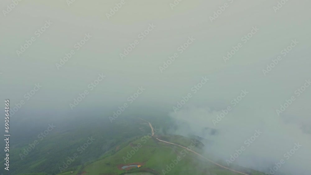 Steppe with green grass covered by misty clouds on a mountain in the middle of a tropical forest with an aerial view from a drone.