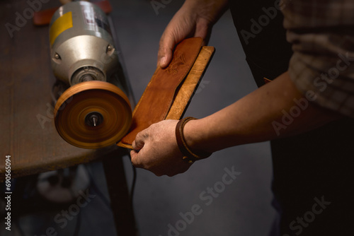 tailor making perfect edge for leather. close up cropped side view photo. craftsman using a machine burnisher, man customing leather phone case. man makes cell phone case