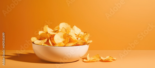 Golden potato chips in a white bowl on a dual-tone orange and beige background, shadow play.